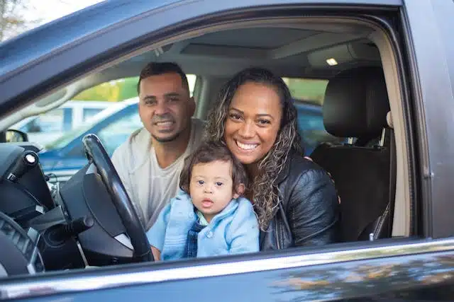 A family of three smiling in a vehicle. 